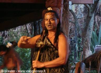 Maori man with facial tattoos and woven cloak performs haka among the trees