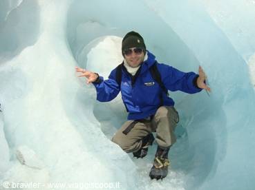 Hiker in blue jacket crouching inside a glacial ice cave