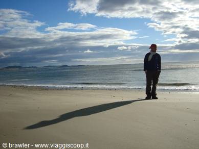 Man standing on a sandy beach, low light, scattered clouds over the sea