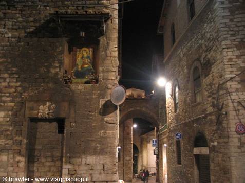 Medieval stone alley at night, frescoed shrine lit beneath a tower
