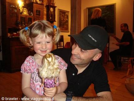 Blonde girl with pigtails holding a doll, smiling man in black cap beside