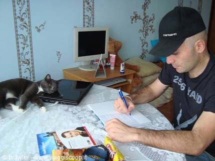 A man writes in a notebook while a cat sleeps next to the laptop