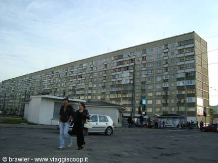 Two people crossing the square in front of a huge grey apartment block