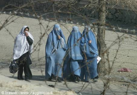Women in blue burqas walk beside barbed wire on a street