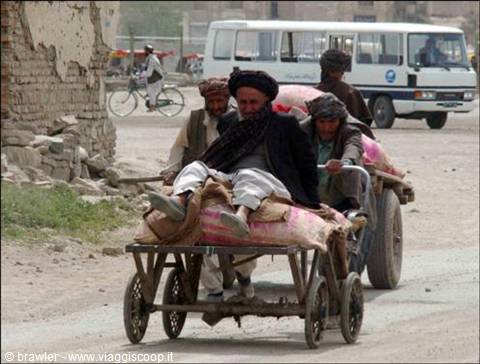 Men in turbans on a wooden cart, one pushing, white bus behind