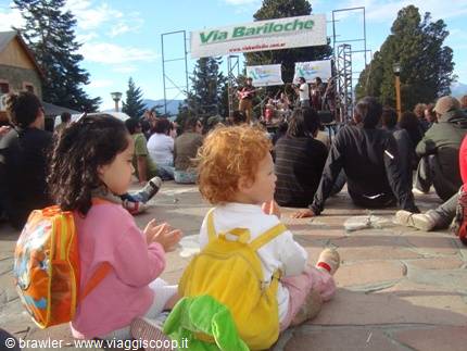 Toddlers with backpacks sitting on stone square facing stage in Bariloche