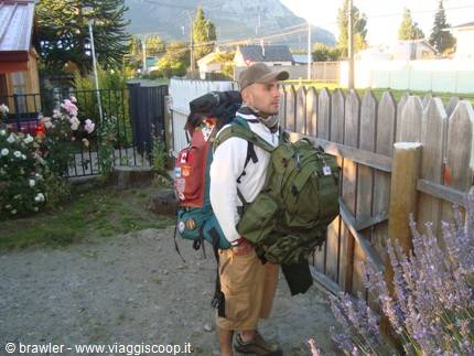 Traveler with backpack and green duffel bag beside a wooden picket fence