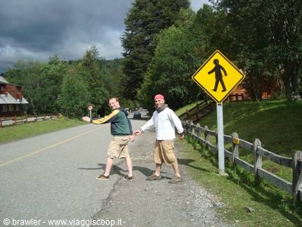 Two tourists crossing a country road next to a yellow pedestrian sign
