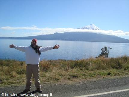 Traveler with open arms on roadside, lake and snow-capped volcano behind