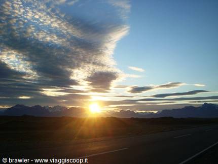 Low sun over asphalt road, dark mountains and streaked clouds in Patagonia