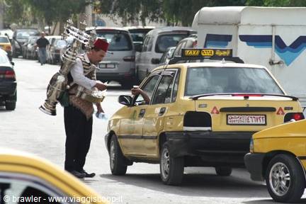 Tea vendor with brass kettles serves a yellow taxi driver in Tunis