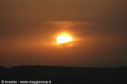 Golden sun behind clouds above dark hills silhouetted at dusk