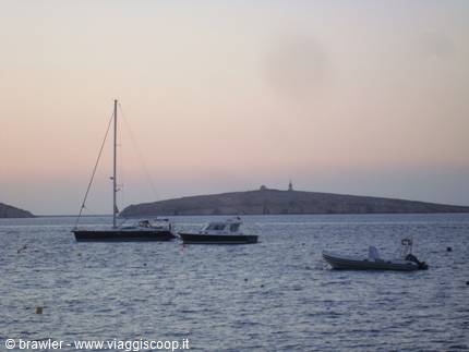 Boats anchored in front of an island with a lighthouse in pink dawn light