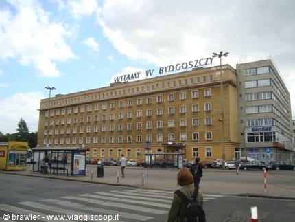 A tourist crosses the street in front of a large yellow building, Bydgoszcz