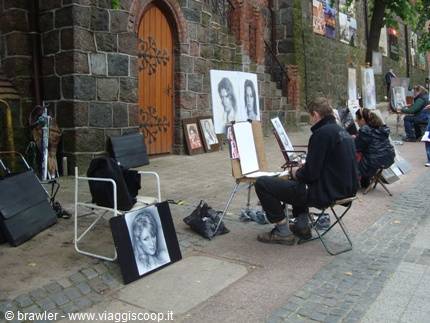 Portrait artist sketching on easel beside a stone church wall