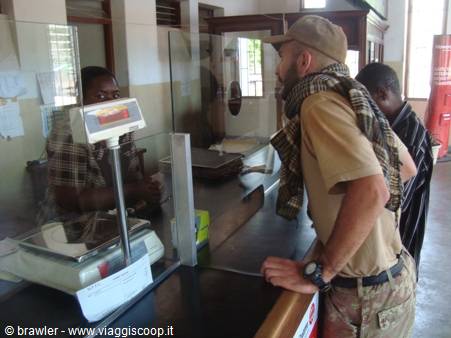 Traveler with scarf at ticket counter, luggage scale behind the desk