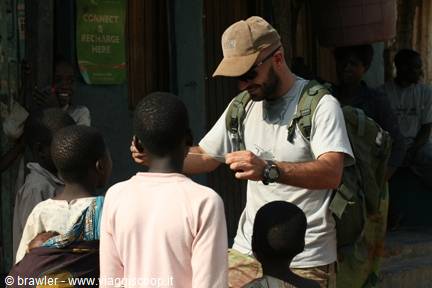 Backpacker with green rucksack shows something to children on an African street