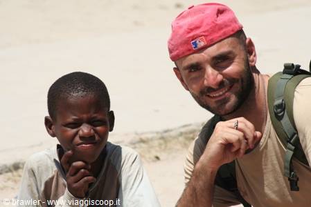Traveler in pink cap and backpack smiling beside a child on sand