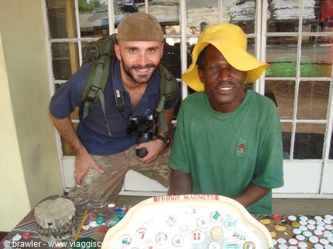Backpacker tourist with camera beside a smiling vendor in yellow hat selling fridge magnets