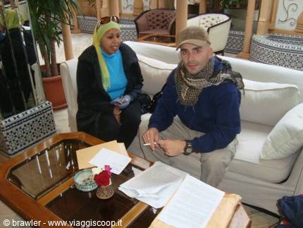 Man wearing keffiyeh and woman in headscarf sitting on hotel lobby sofas