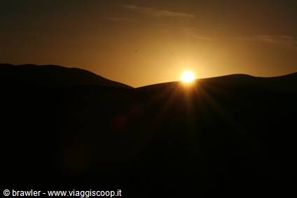 The sun rises behind hills in backlight