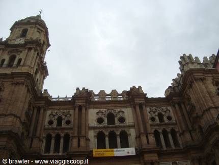 Baroque stone facade of Malaga Cathedral under cloudy sky