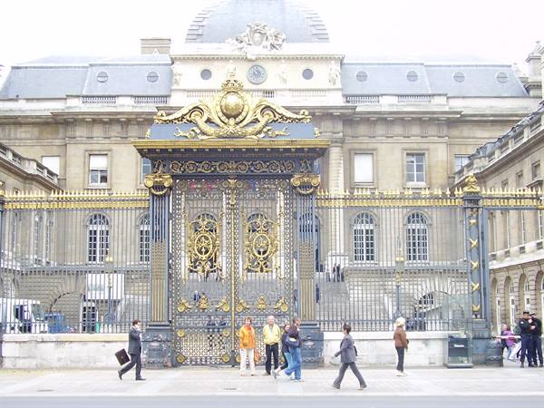 Gilded gate of the Palais de Justice in Paris, pedestrians under soft light