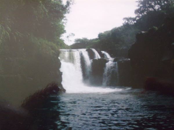 White waterfall over dark rocks amid tropical vegetation, rippling lake below