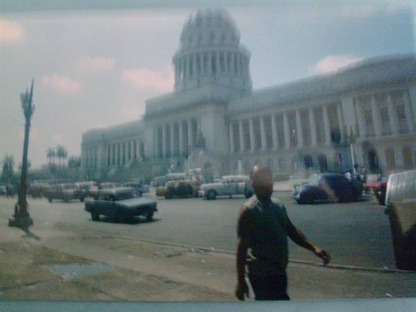 Man crossing the street in front of El Capitolio, Havana, vintage cars passing