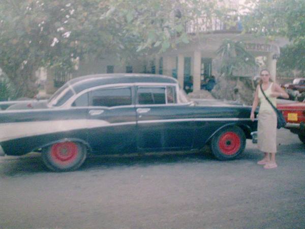 Woman beside a vintage black car with red wheels under the trees