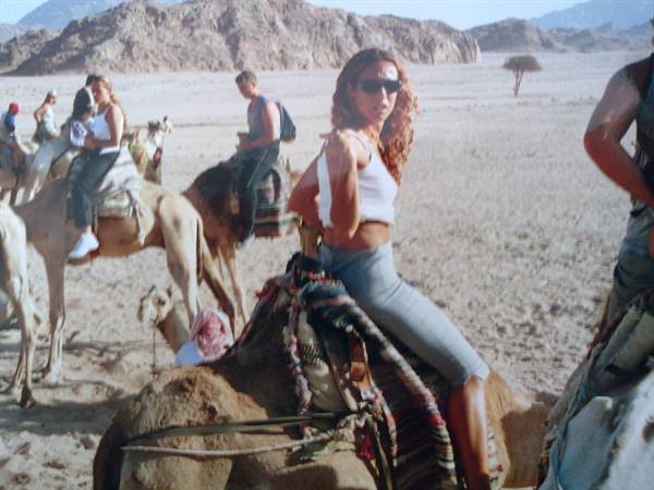 Tourists riding camels in sandy desert with rocky mountains behind