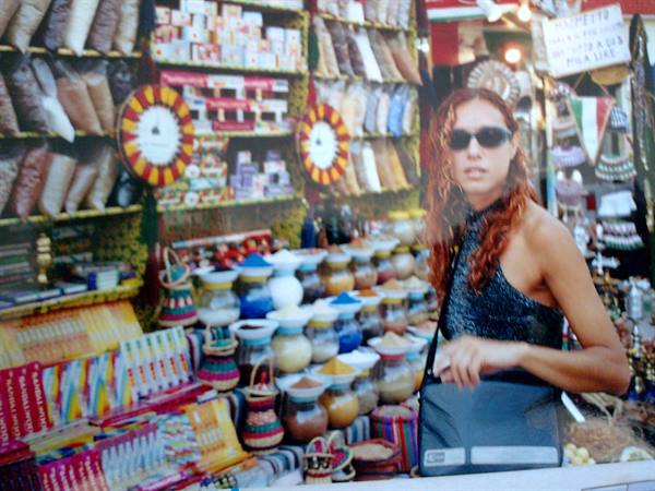 Woman in sunglasses in front of colorful spice stall at bazaar