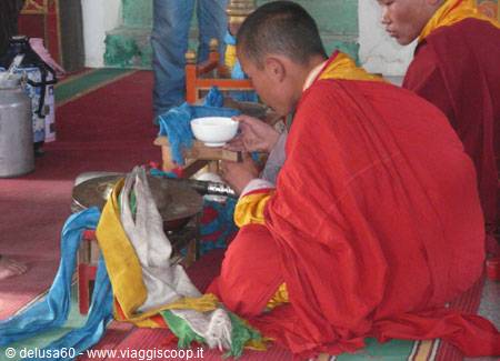 Buddhist monk in red robe drinking tea from a white bowl
