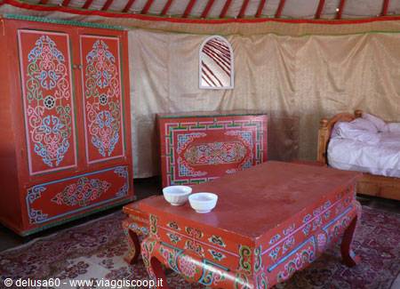 Inside a yurt with painted red wooden furniture and a bed