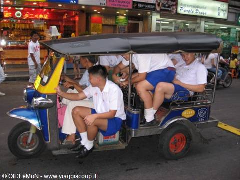 Students in white and blue uniforms crowding onto a blue tuk-tuk on the street