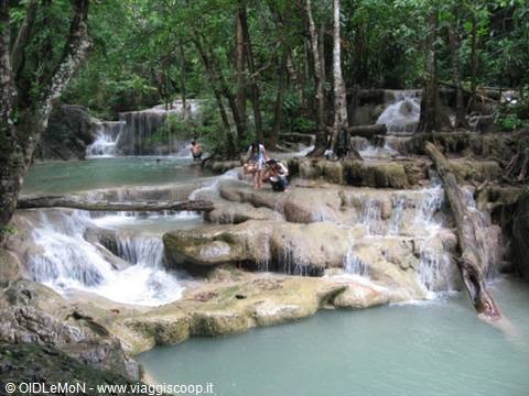Tourists on limestone rocks among Erawan waterfalls, turquoise water and forest