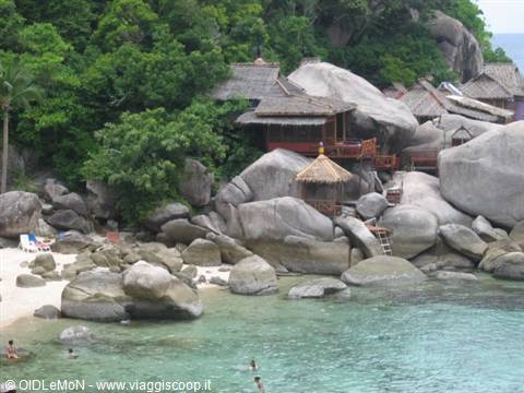 Wooden bungalows with thatched roofs among giant granite boulders, sandy beach and turquoise water