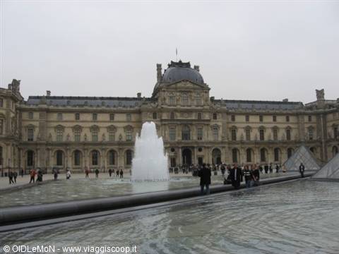 The fountain in the Louvre courtyard in Paris, visitors beside the glass pyramids