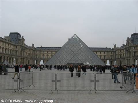 Tourists in the Louvre courtyard in front of the glass pyramid, grey sky