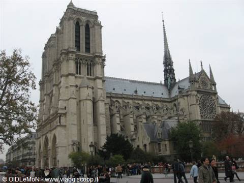 Notre-Dame Cathedral in Paris, light stone under grey sky, tourists strolling by