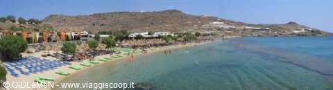 Greek beach with blue and green umbrellas, tavernas and arid hills on turquoise sea