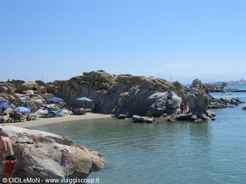 Beach with granite rocks, beach umbrellas and turquoise water, swimmers on boulders