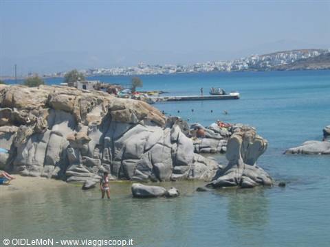Swimmer among smooth grey rocks, turquoise water, wooden pier and whitewashed town