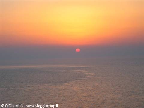 The red sun sinks into the calm sea under an orange sky