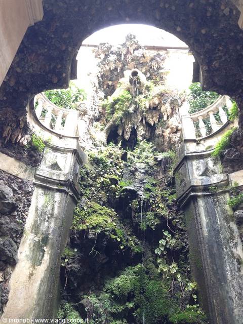 Baroque fountain crusted with moss and shells between stone columns and balustrade