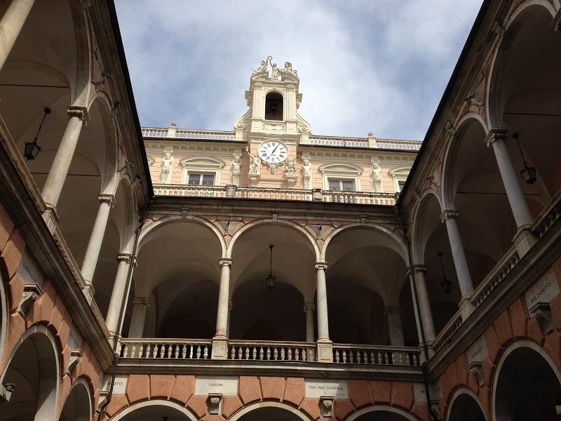 Cortile porticato di Palazzo Doria Tursi, Genova, con orologio e campanile sotto cielo nuvoloso