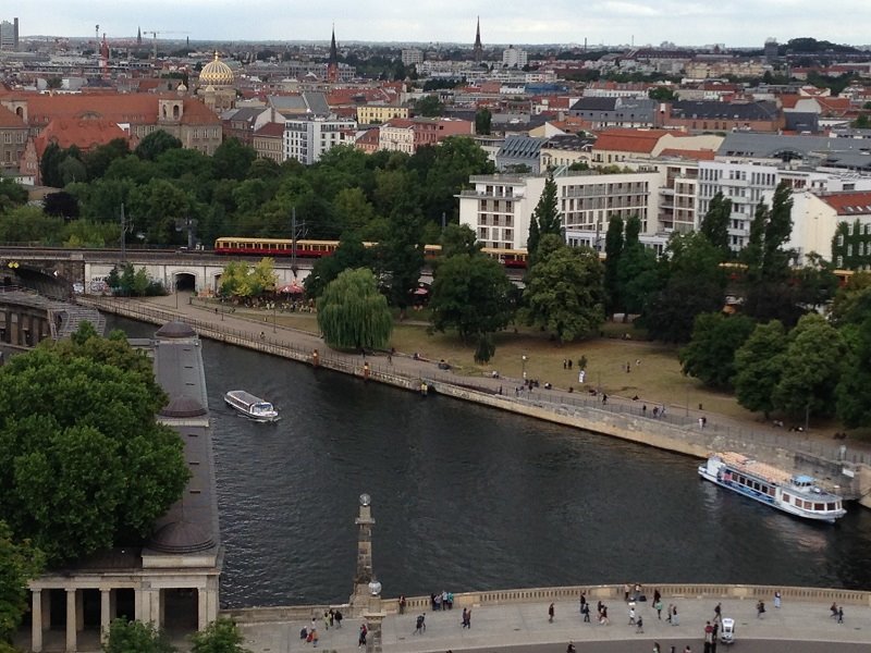 Treno urbano rosso lungo la Sprea, battelli e passanti sul lungofiume a Berlino