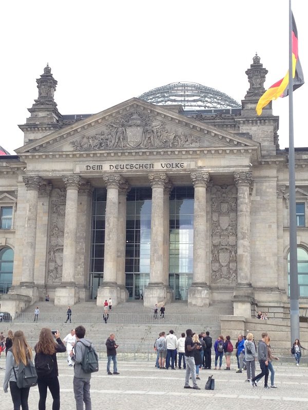 Turisti davanti al Reichstag di Berlino, colonne in pietra e bandiera tedesca al vento