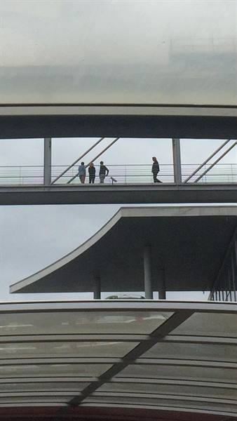 People walk on an elevated glass walkway between modern steel structures