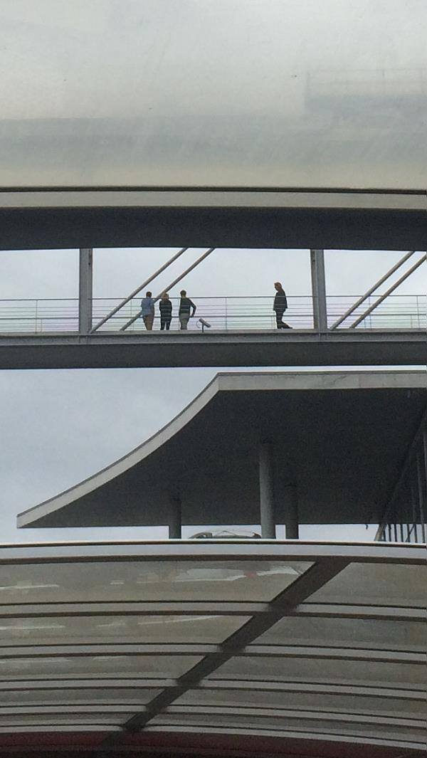 Persone camminano su una passerella vetrata tra strutture moderne di acciaio